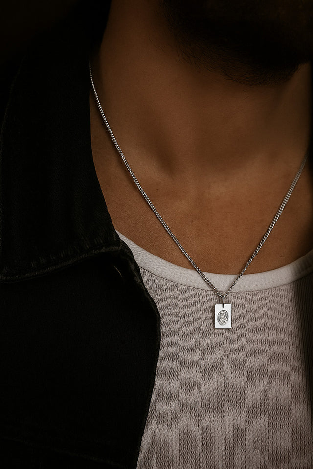 Man som bär ett halsband i silver med graverad berlock som har fingeravtryck.