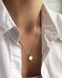 Kvinna som bär ett silverhalsband med berlock med diamantbokstav.  