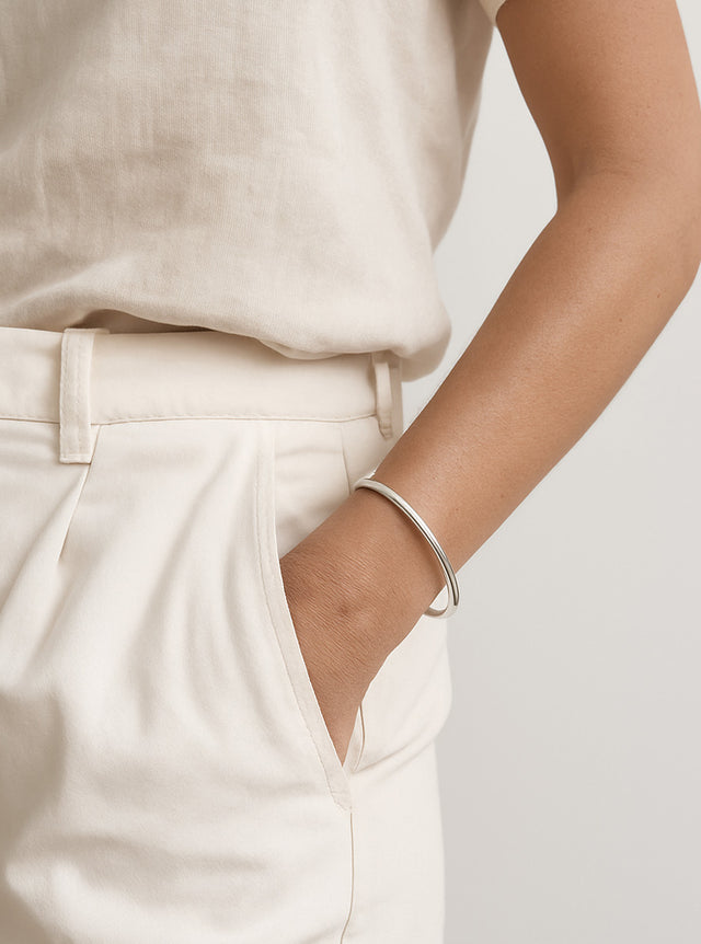 kvinna som bär ett stelt silverarmband med slät yta. 