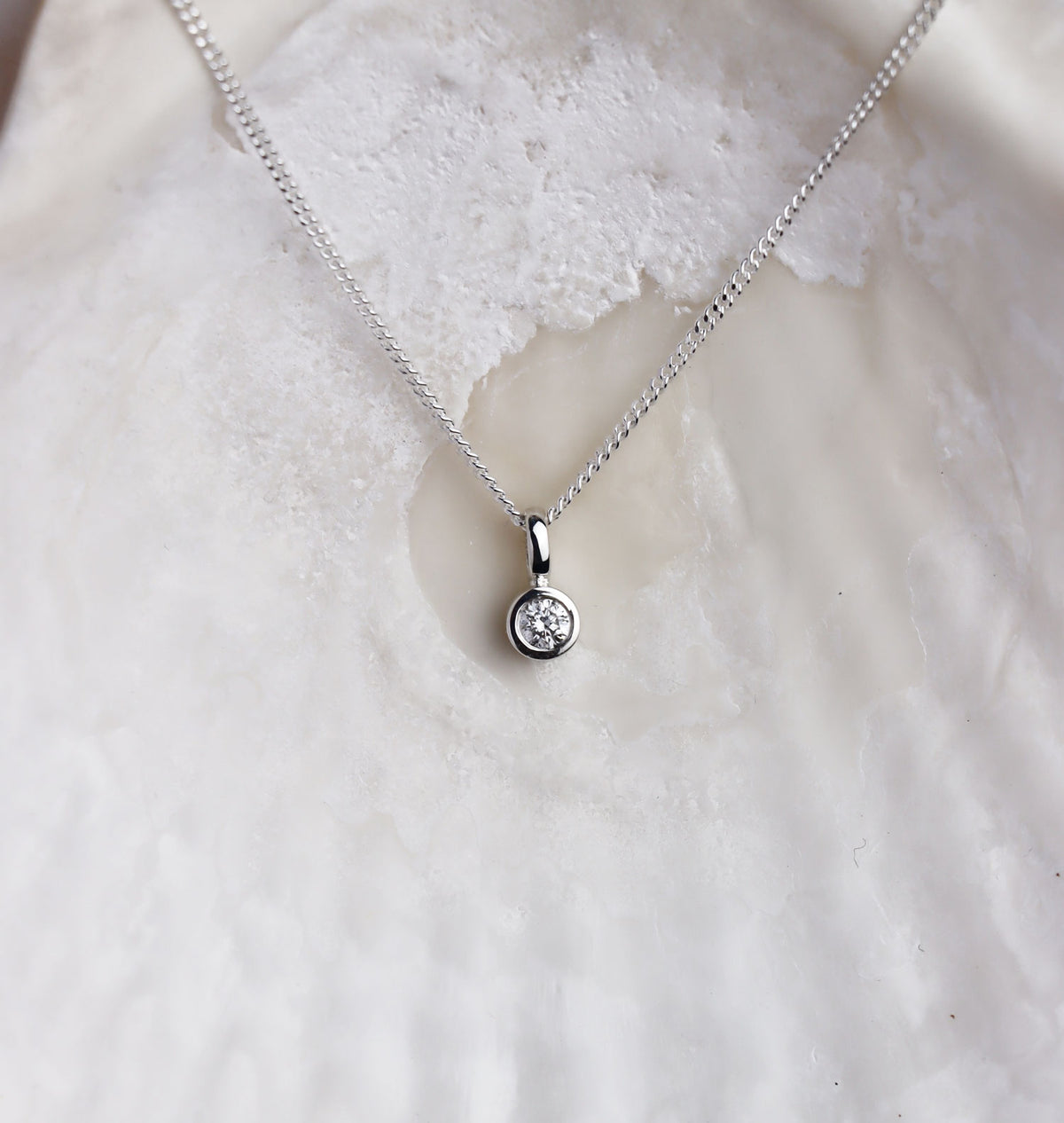 Närbild på ett diamant hängsmycke i kedja med en gnistrande diamant i silverfattning utformad som ett rör. 