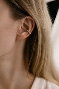 tjej som bär ett ensamt örhängen en bit upp på örat. en ear cuff i silver med små silverkulor. 
