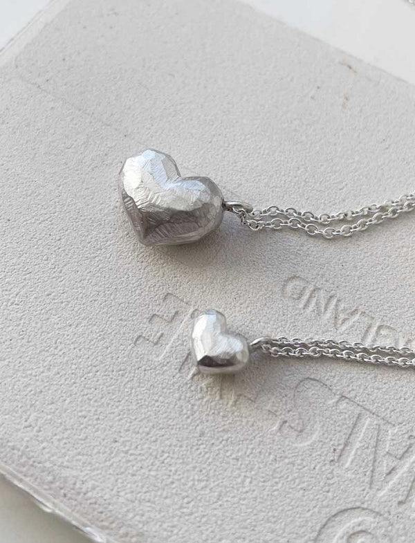 Två halsband med silverhjärtan som har matt, slipad yta.