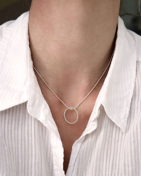 Ett kort halsband i silver med en silverring som hänger i en kulkedja. 