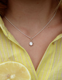 Tjej som bär ett kort silverhalsband med en liten sol. 