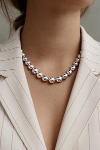 tjej som bär ett halsband med stora länkade silverkulor till vit kavaj . 