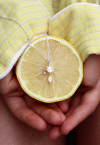 Silverhalsband med en liten sol placerad på en uppskuren citron som hålls mellan två händer. Citrongul skjorta. 
