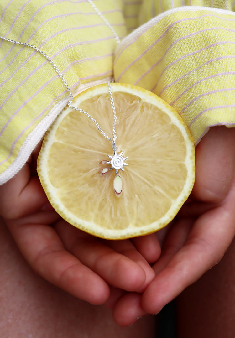 Silverhalsband med en liten sol placerad på en uppskuren citron som hålls mellan två händer. Citrongul skjorta. 
