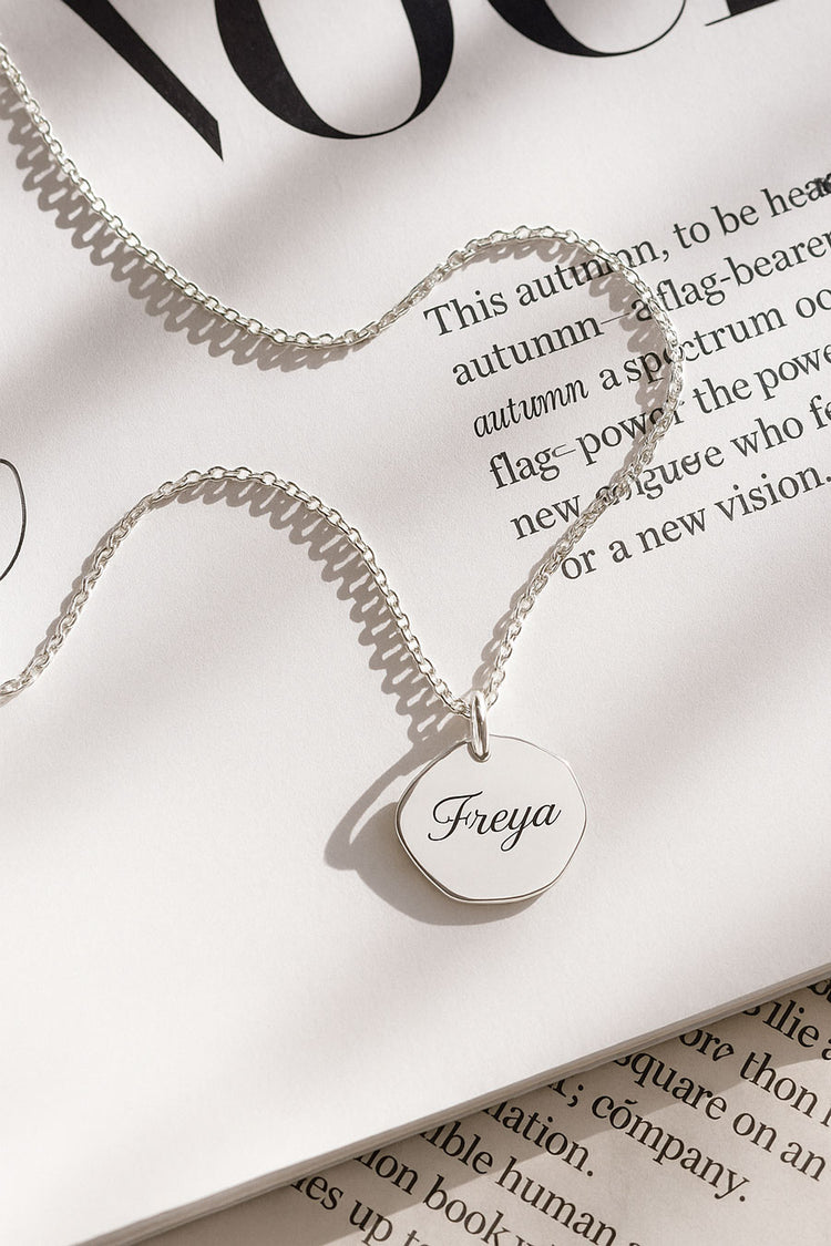 halsband med graverat namn på en berlock i silver, placerad på ett magasin. 