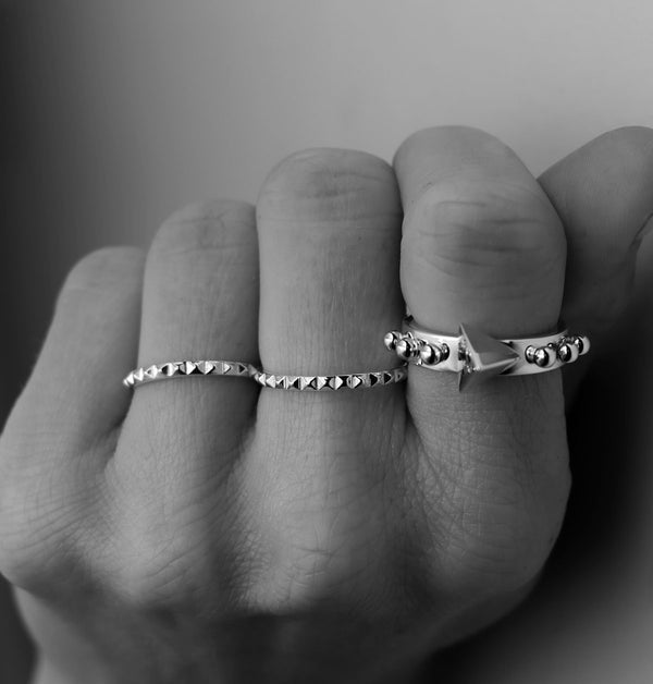 Hand som bär tre silverringar på olika fingrar, alla ringar har nitar. 