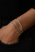 tre silverarmband i kombination på en arm. ett armband med silverkulor, en slät kedja och ett stelt silverarmband. 