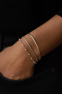 tre silverarmband i kombination på en arm. ett armband med silverkulor, en slät kedja och ett stelt silverarmband. 