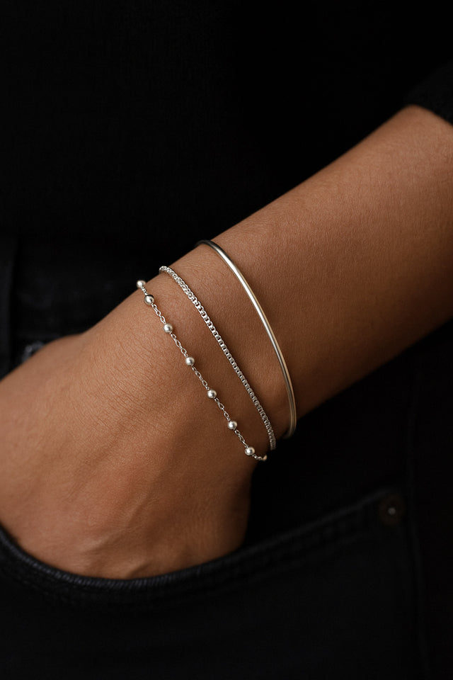 tre silverarmband i kombination på en arm. ett armband med silverkulor, en slät kedja och ett stelt silverarmband. 