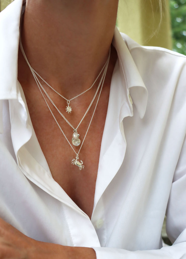 Kvinna som bär tre silverhalsband i olika längder. En liten sol, en snäcka och en krabba i silver. 
