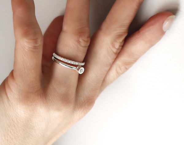 Två ringar i kombination. En diamantring med ett band av diamanter och en ring med en diamant i tub. 
