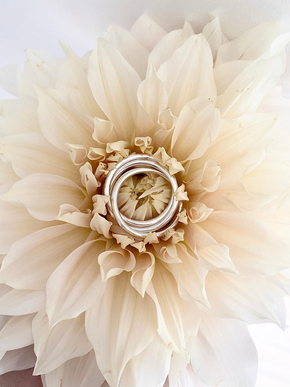 Silverring med tre ringar i en ring. Ringen är placerad på en vit blomma. 