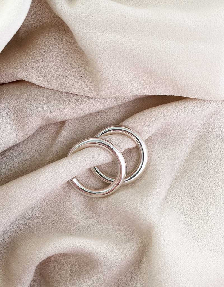 Ett par örhängen med blanka silverringar, placerade på ett beige tyg. 